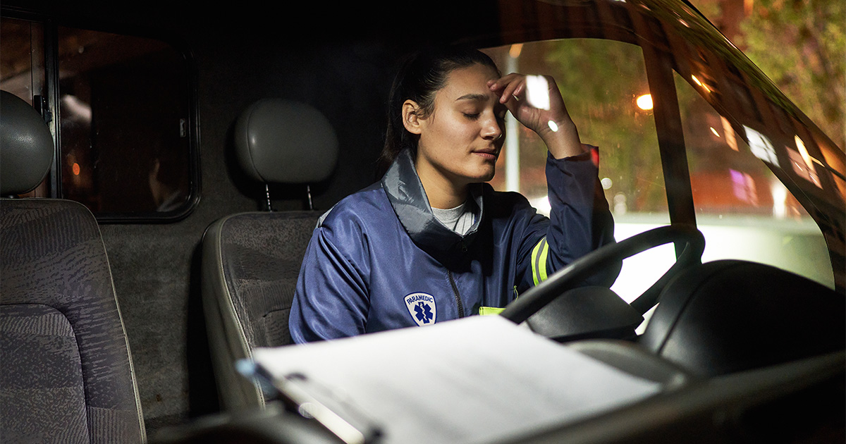 a stressed female paramedic sits in an ambulance